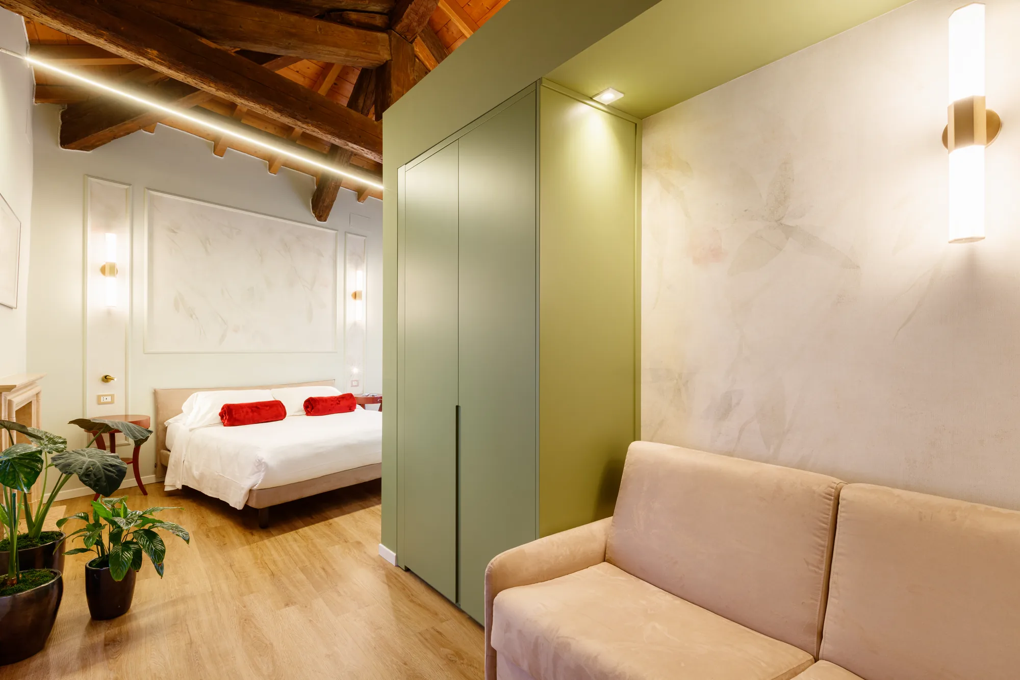 Una camera da letto moderna con soffitto in legno, letto matrimoniale con coperte rosse, armadio verde e divano beige