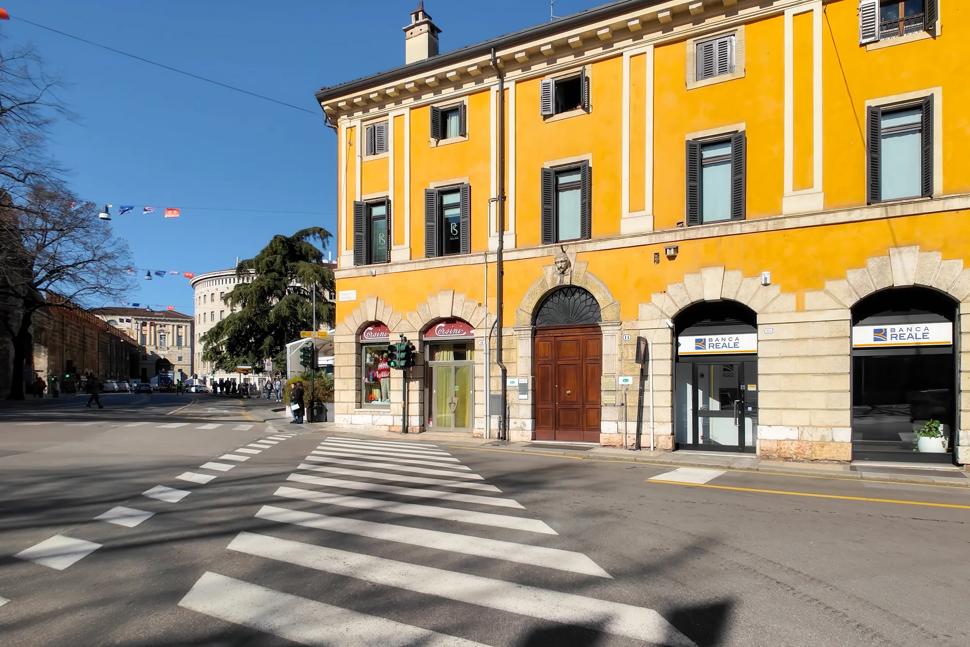 Incrocio con strisce pedonali, edificio giallo con negozi e una banca, sotto un cielo sereno