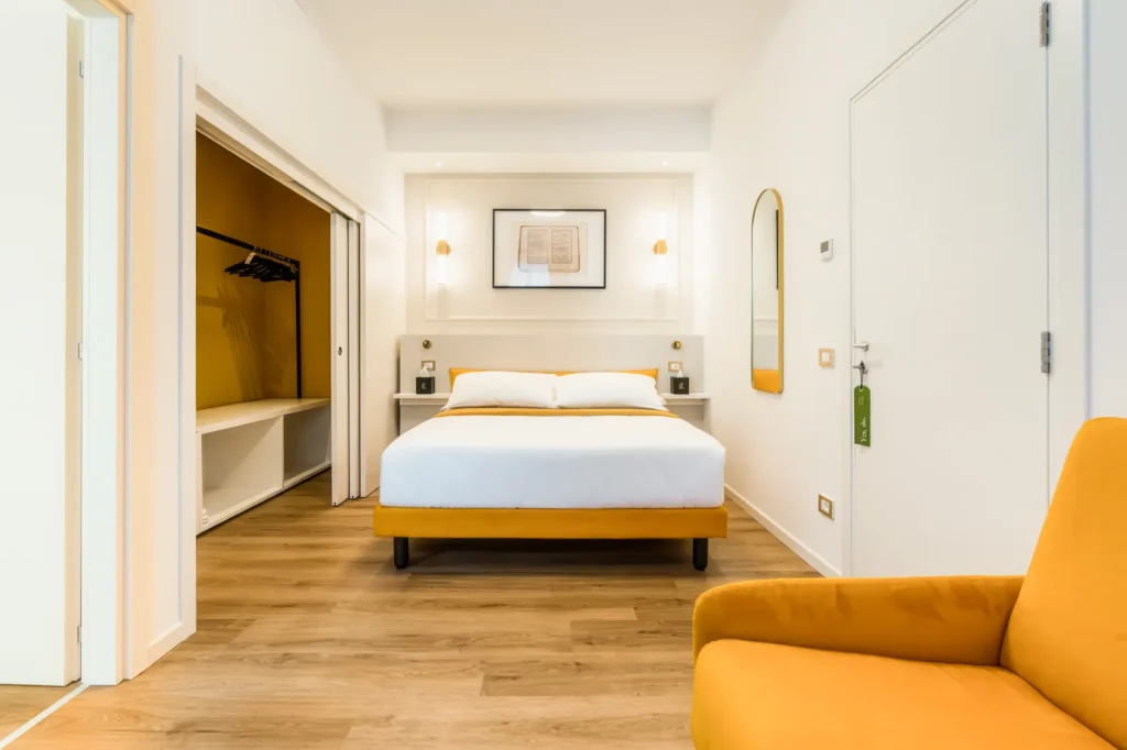 Camera da letto moderna con letto matrimoniale, armadio, specchio e poltrona gialla. Pareti bianche e pavimento in legno