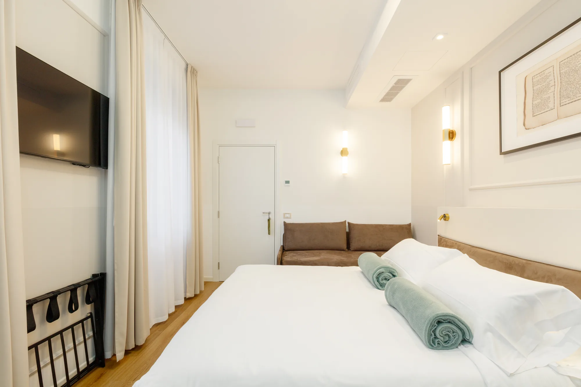 Camera con letto matrimoniale, divano, TV a parete e tende chiare