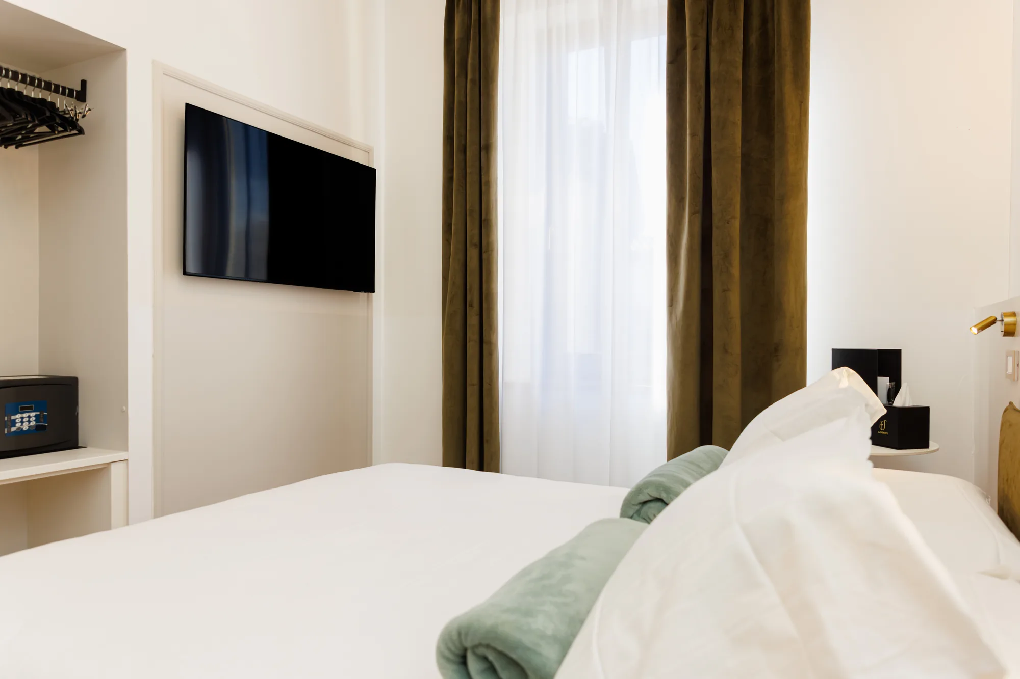 Camera da letto con un letto bianco, un televisore a parete, tende verdi e un comodino con oggetti
