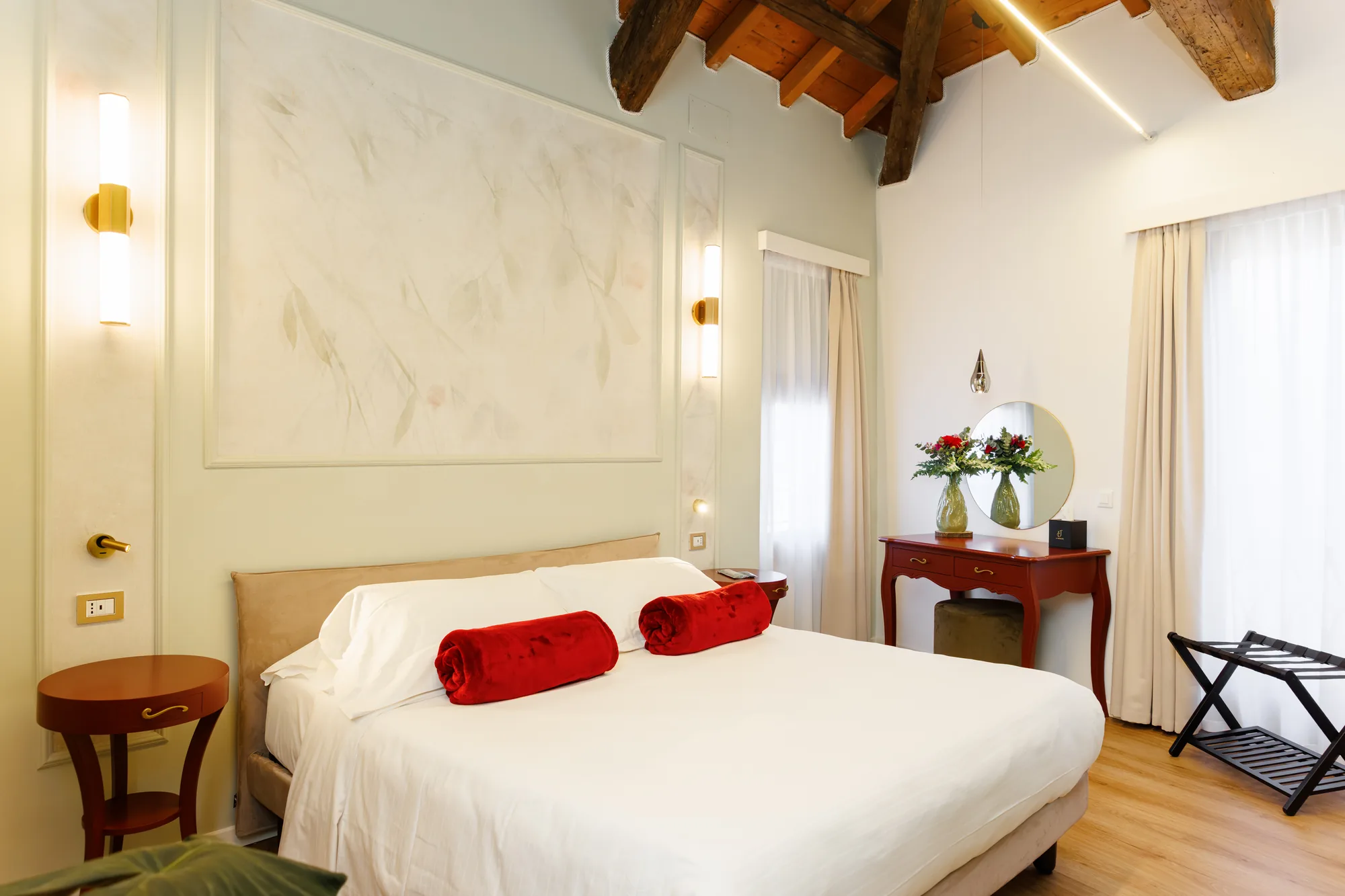 Camera da letto elegante con letto matrimoniale, cuscini rossi, tavolino, specchio e decorazioni floreali