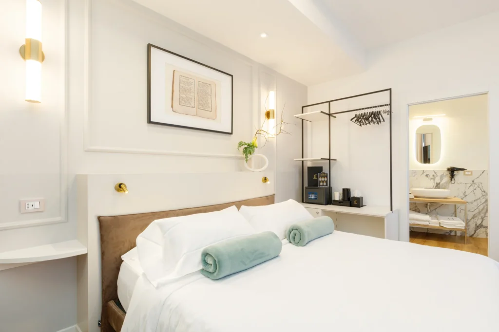Camera da letto elegante con letto matrimoniale, biancheria bianca e asciugamani arrotolati. Armadio e bagno visibili