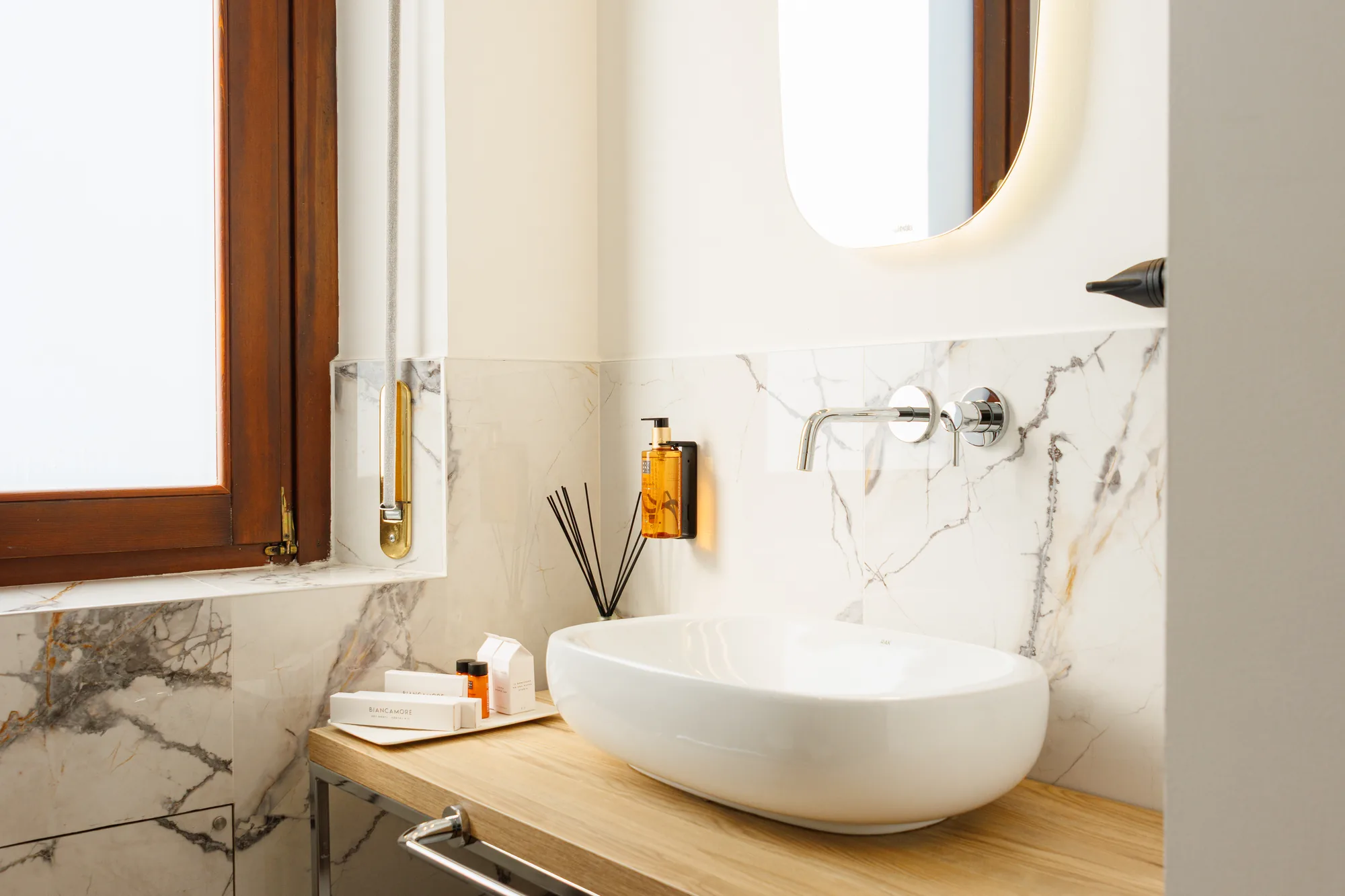 Un bagno moderno con lavabo bianco, rubinetti cromati, prodotti per la cura e una finestra in legno