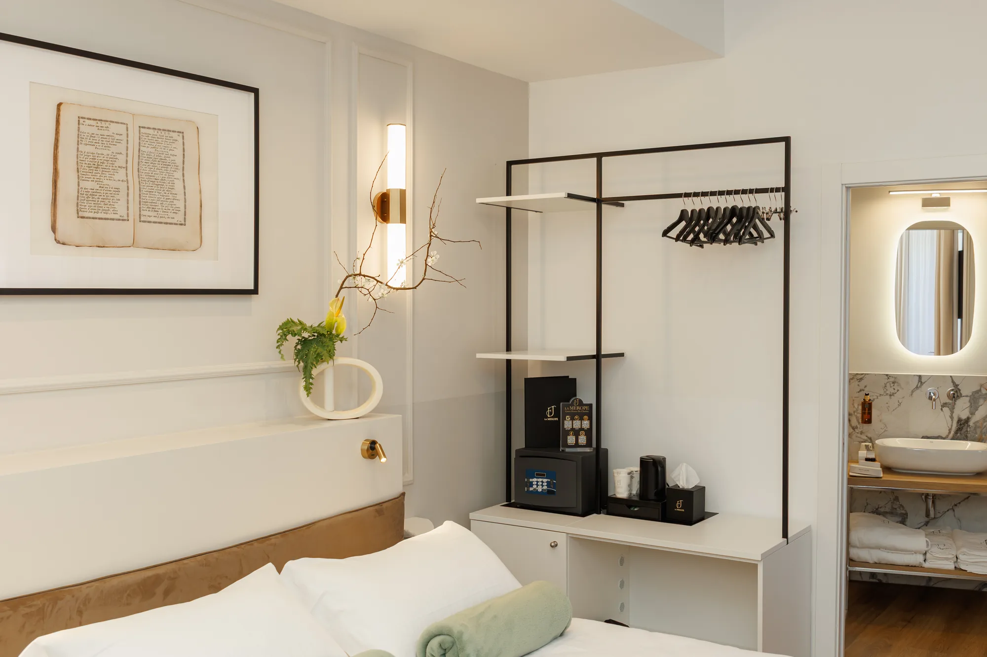 Camera da letto elegante con un quadro appeso, un armadio con appendiabiti, un mini frigorifero e un bagno visibile