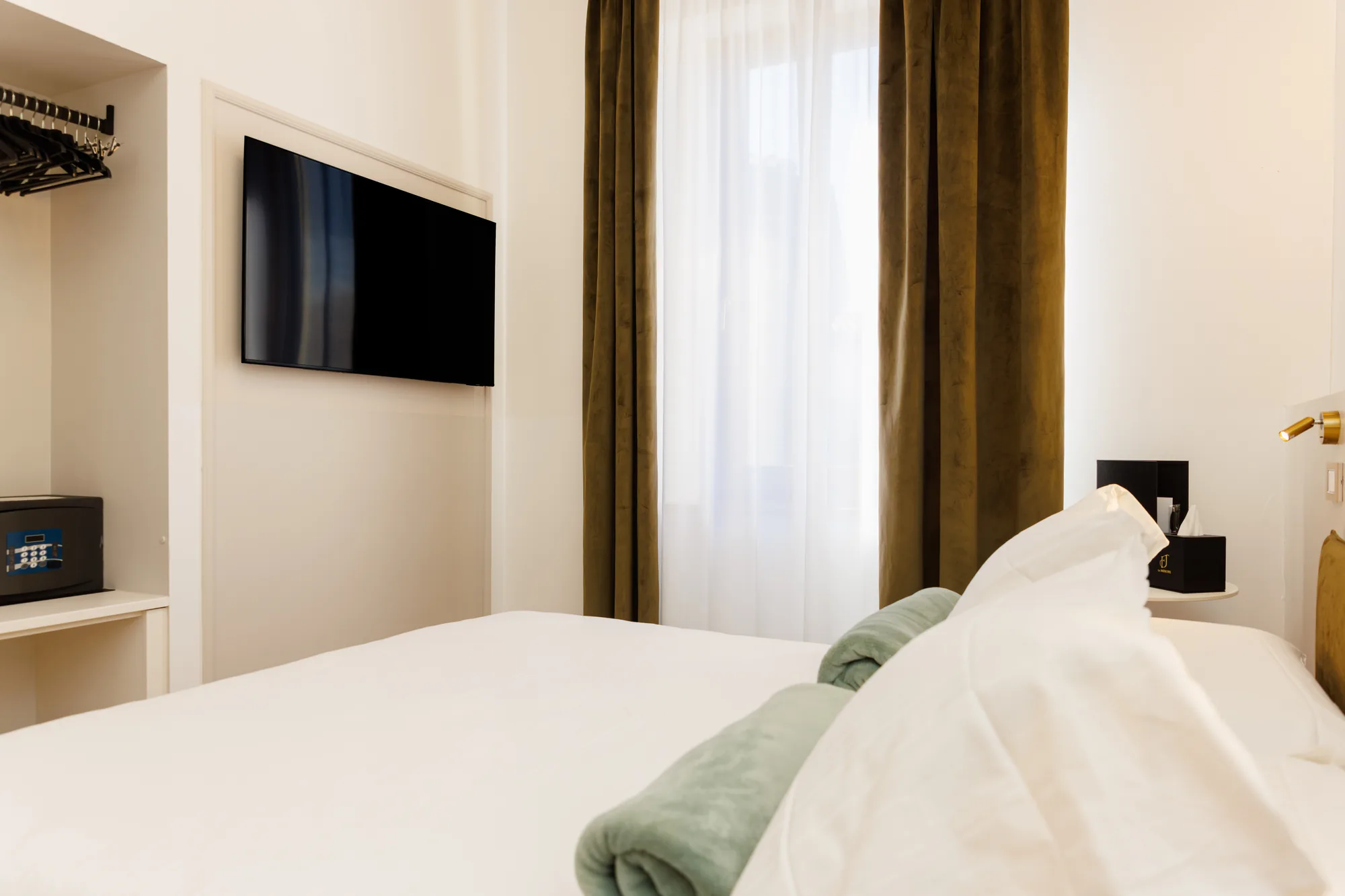 Camera da letto con un letto bianco, un televisore a parete, tende verdi e un comodino con oggetti