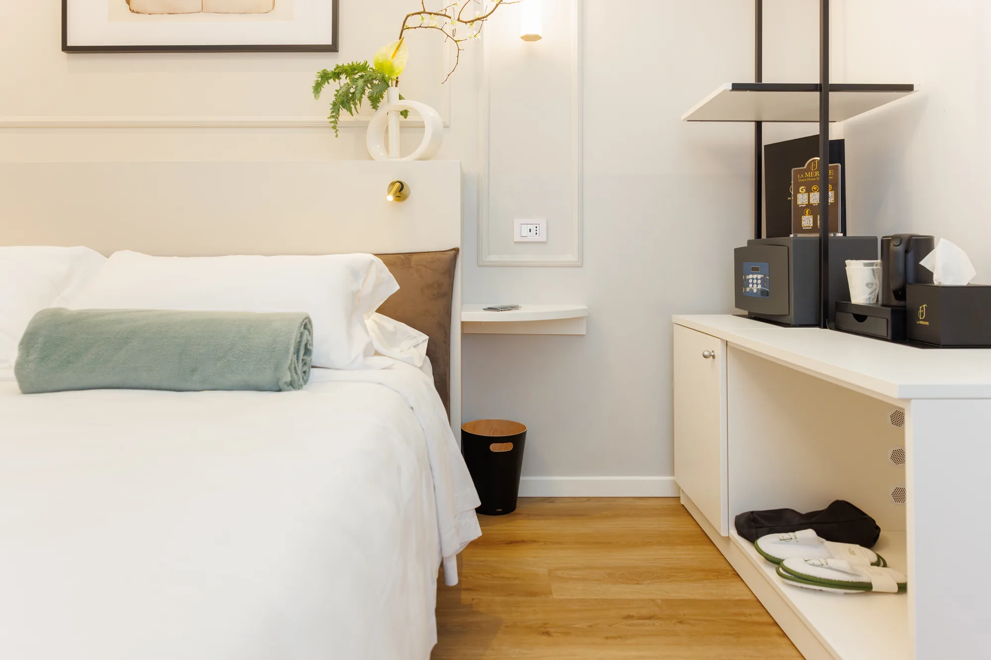 Camera da letto con un letto matrimoniale, un asciugamano arrotolato e un'area di lavoro con macchina per il caffè e ciabatte
