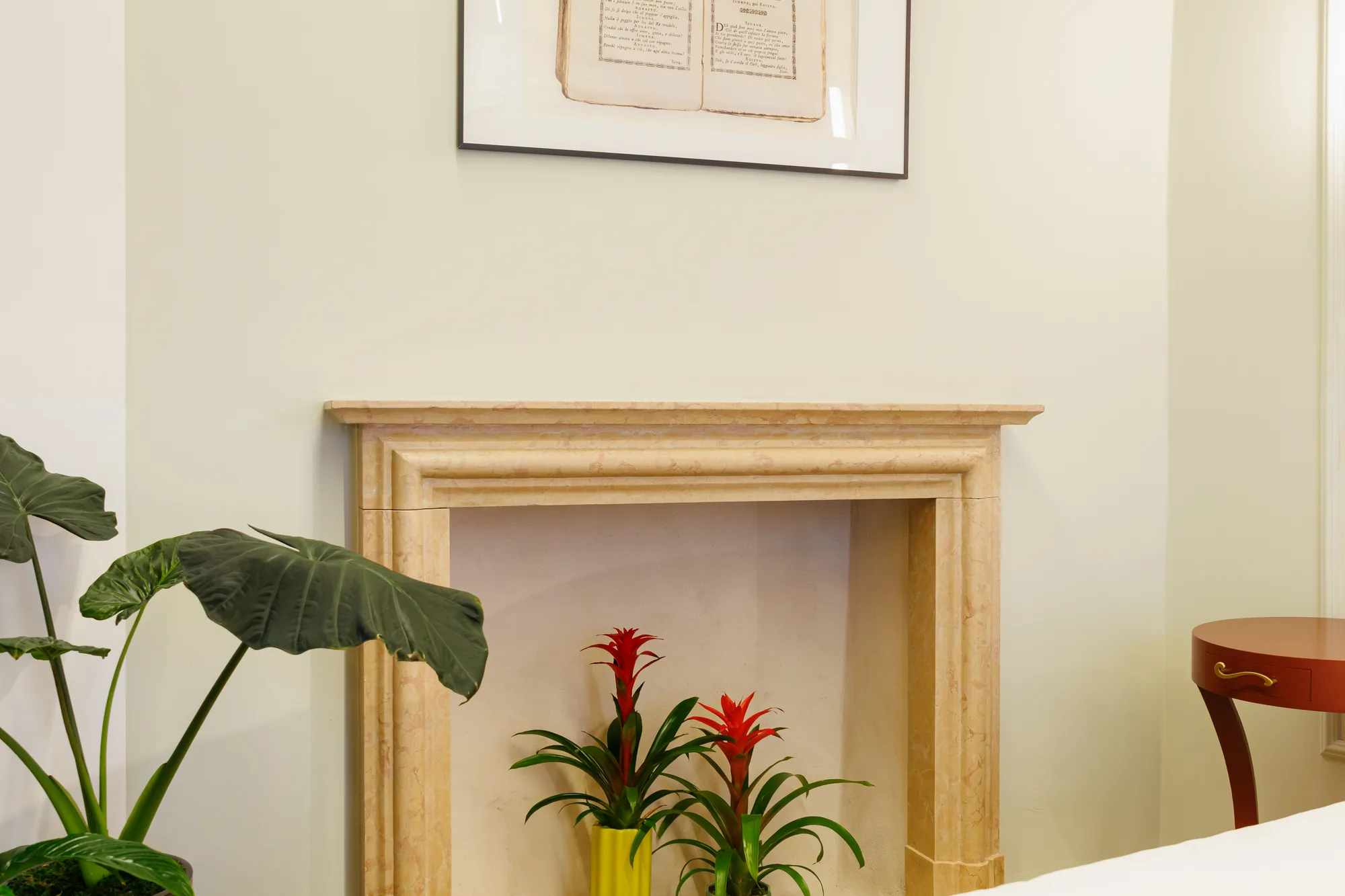 Un camino in marmo con piante decorative e un quadro appeso sopra, all'interno di un ambiente luminoso