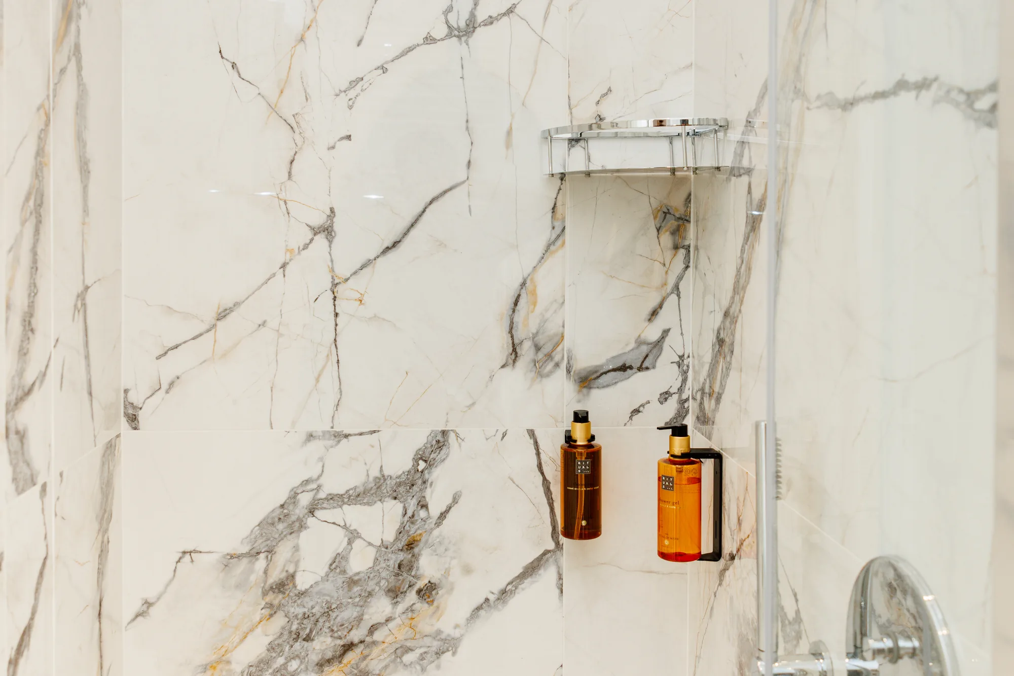 Doccia con muro in marmo e 2 boccette di shampoo e bagnoschiuma
