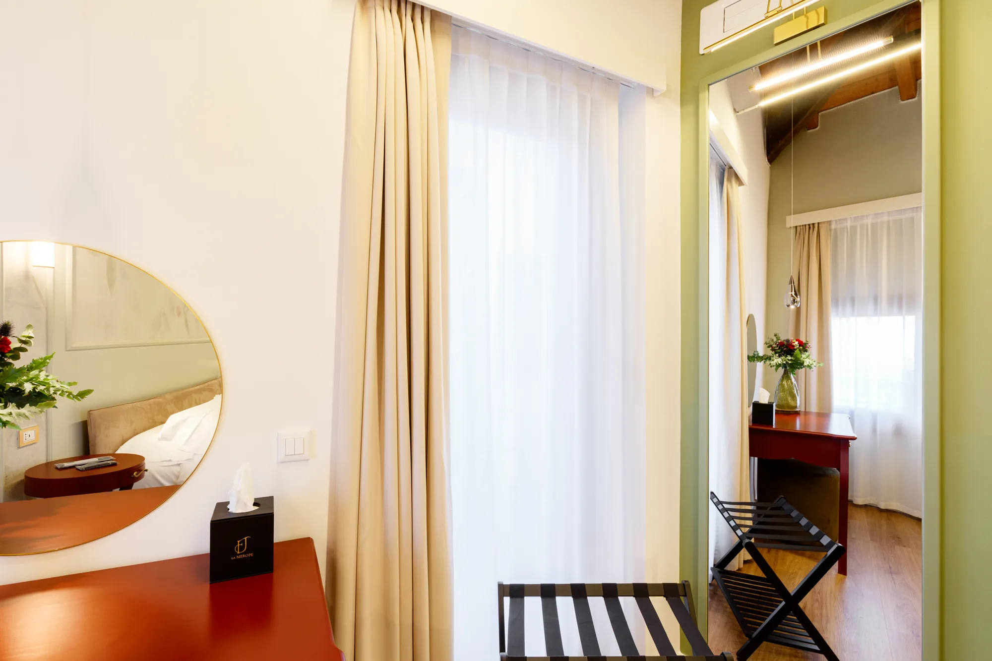 Descrizione di un angolo di una camera d'albergo con un tavolo, una sedia pieghevole, un grande specchio e tende chiare