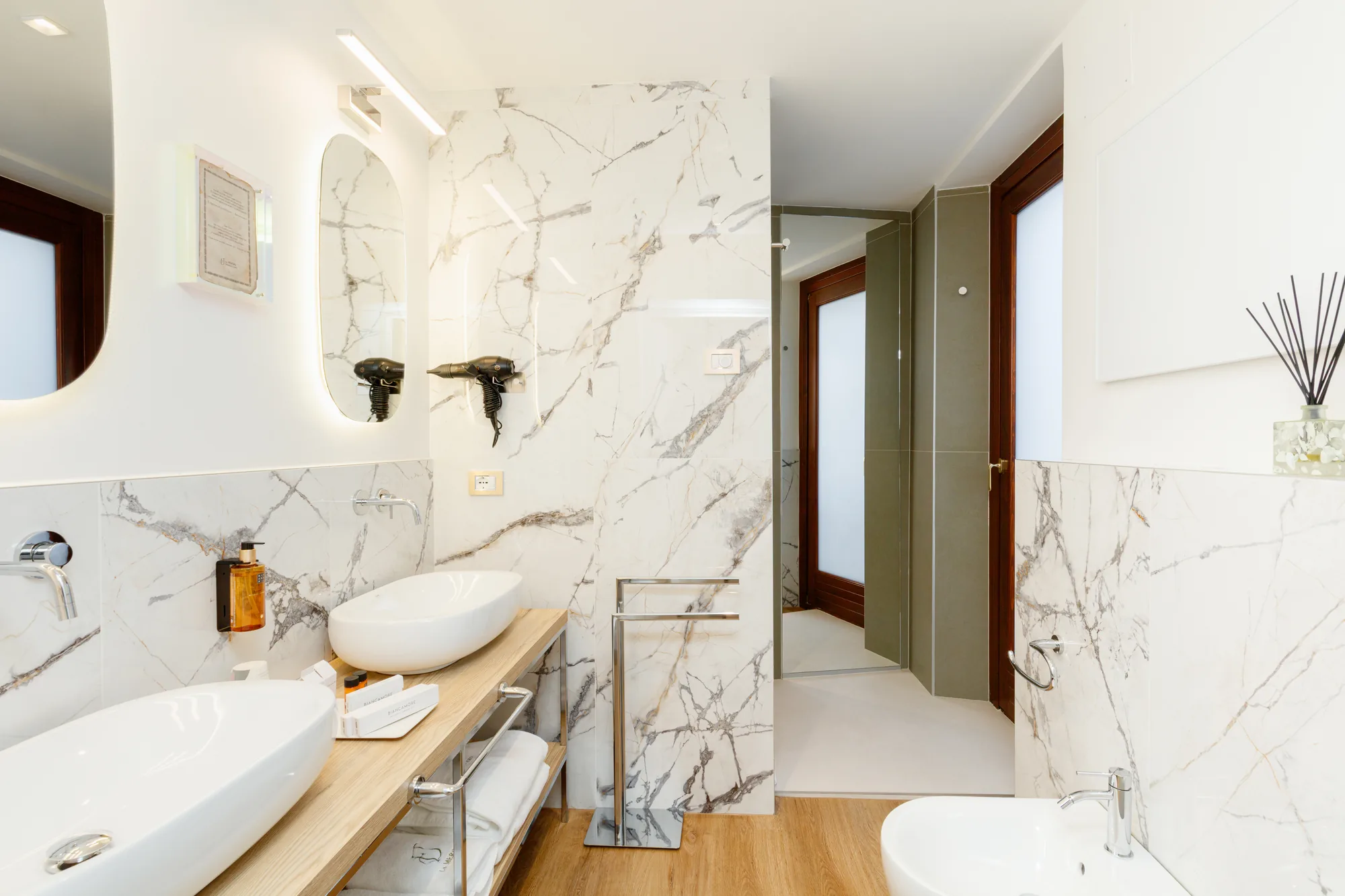Un bagno moderno con pareti in marmo, due lavabi ovali, un asciugacapelli a parete e accessori eleganti